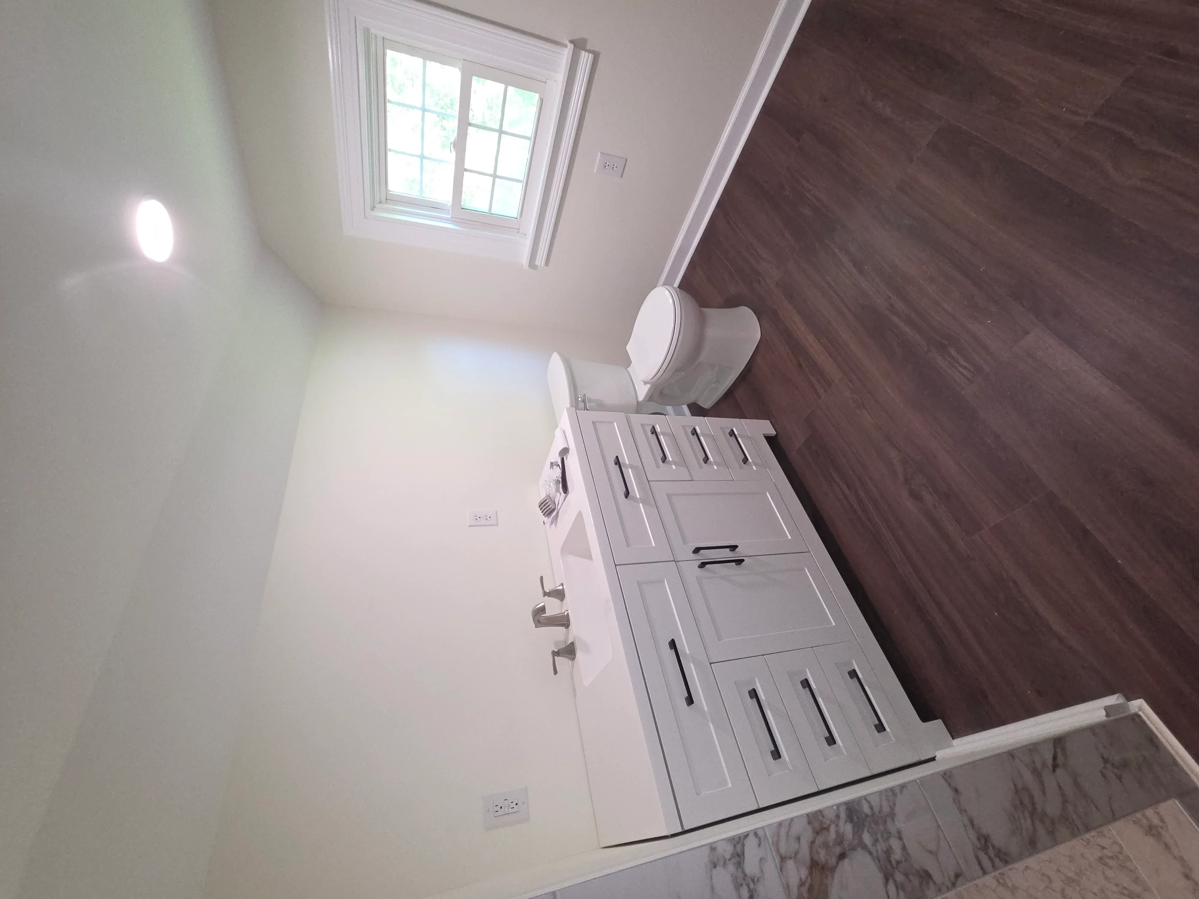 Modern bathroom with white cabinetry, dark wood flooring, and skylight window