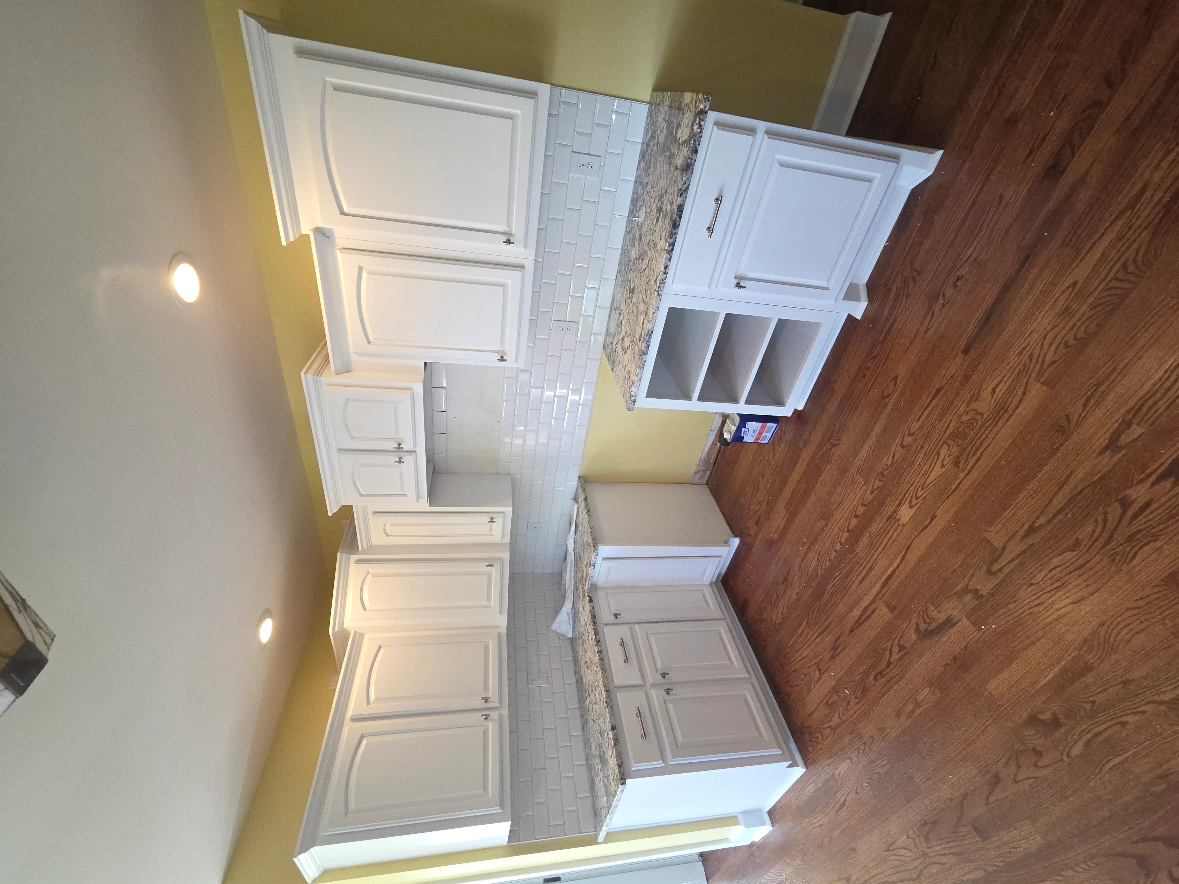 Kitchen with white cabinetry, granite counters, subway tile backsplash, and hardwood floors