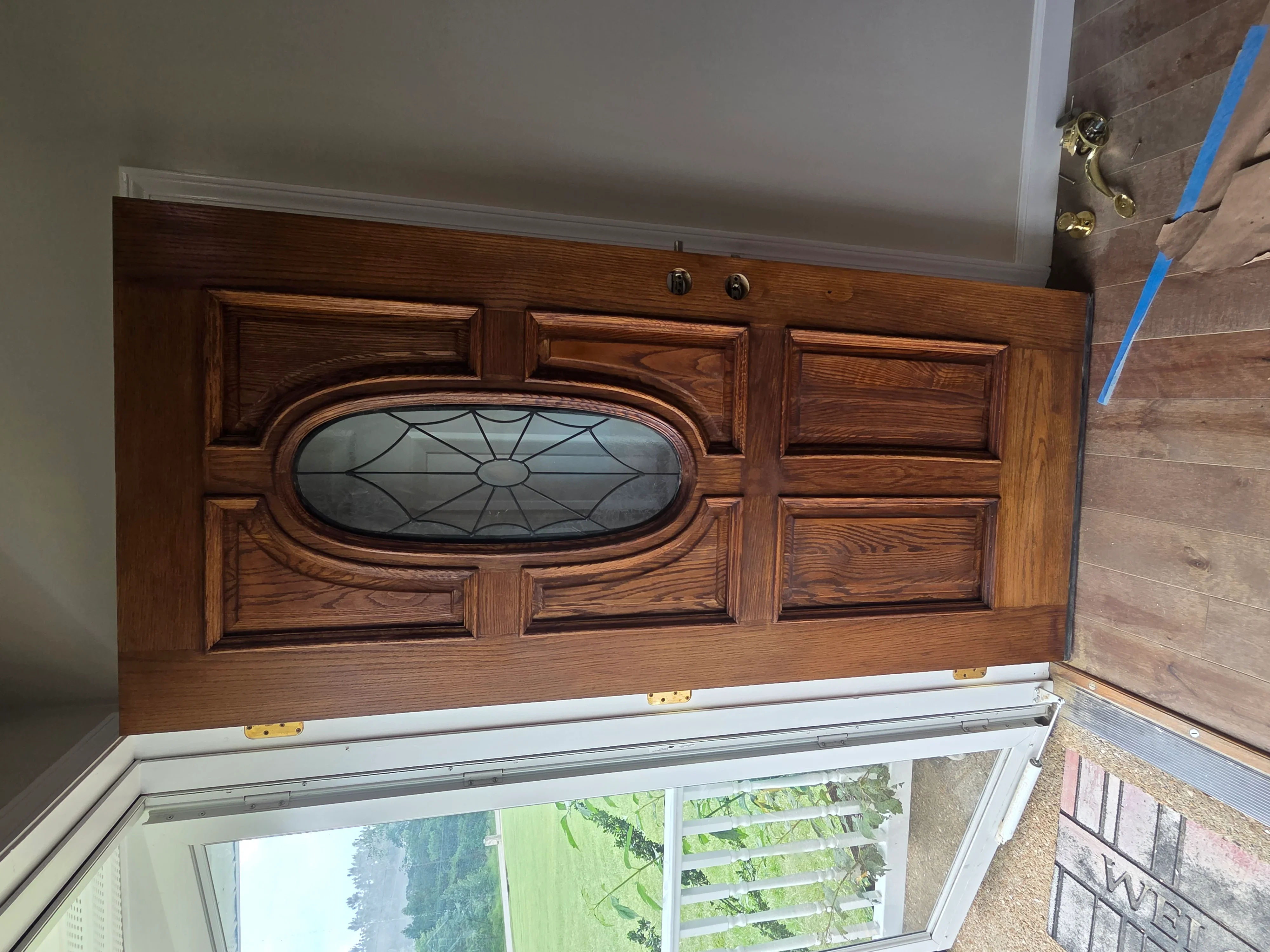 Custom wood entry door with oval glass insert and detailed panel design in warm wood tone