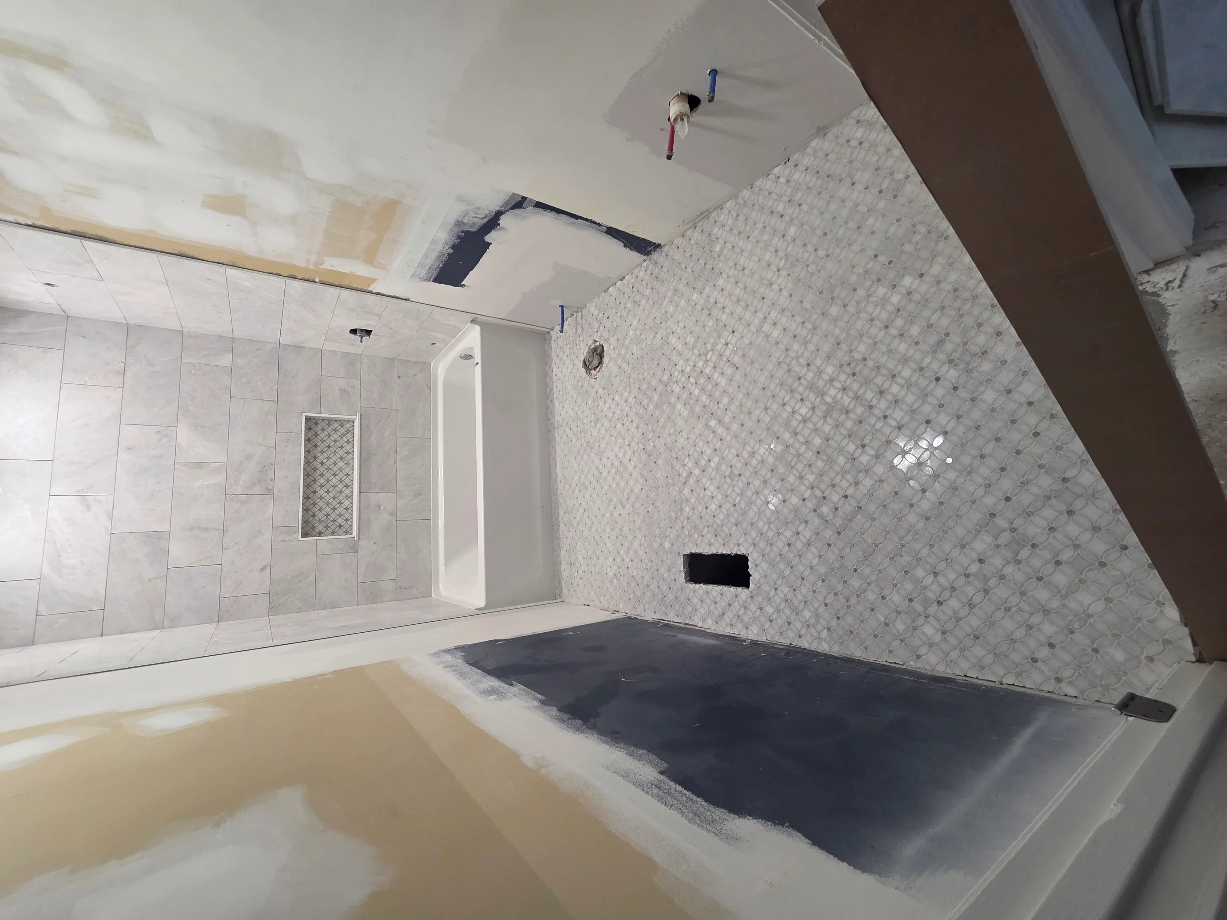 In-progress bathroom remodel showing tiled shower walls, glass enclosure, and ceiling work