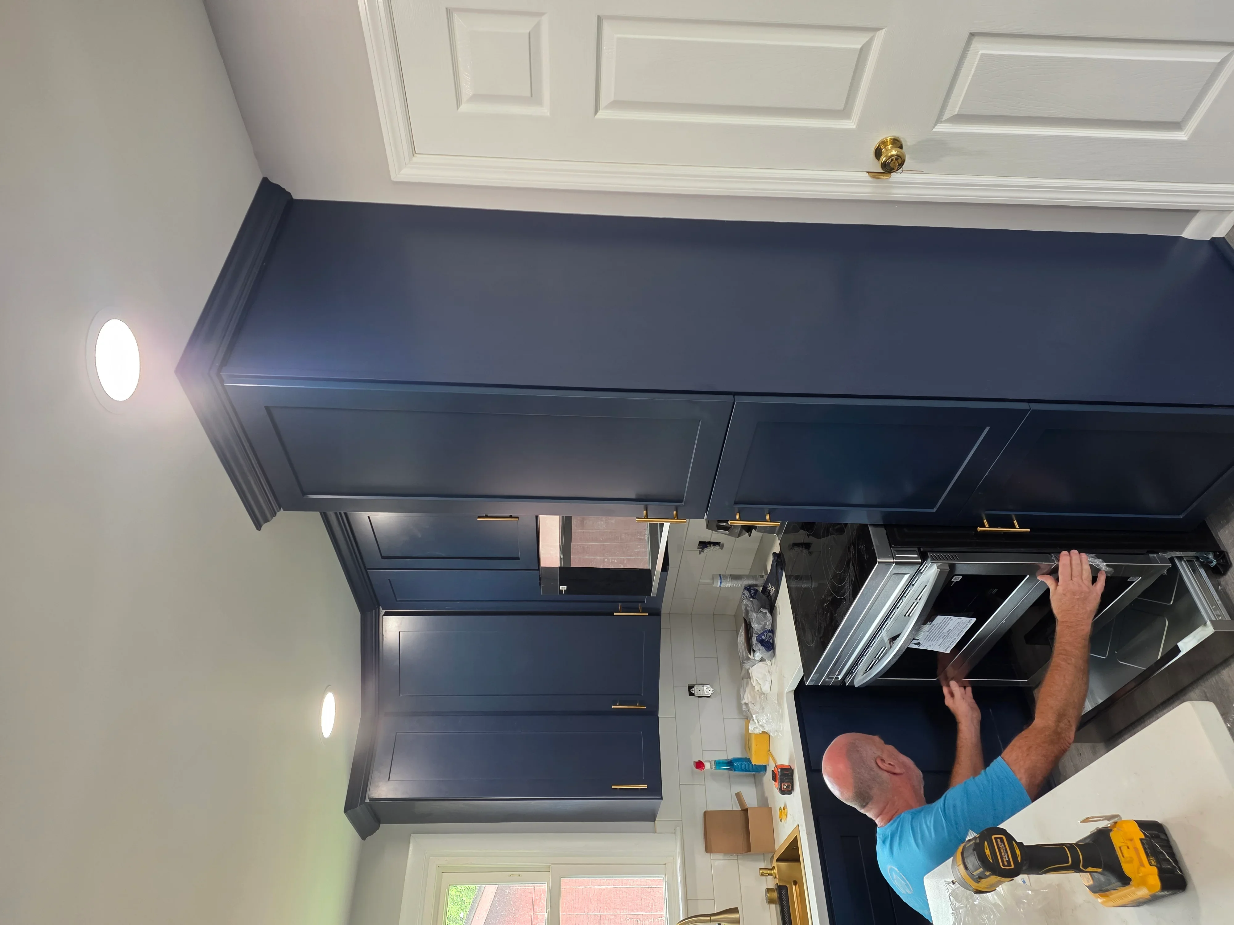 Navy painted kitchen cabinets with brass hardware and recessed lighting installation in progress