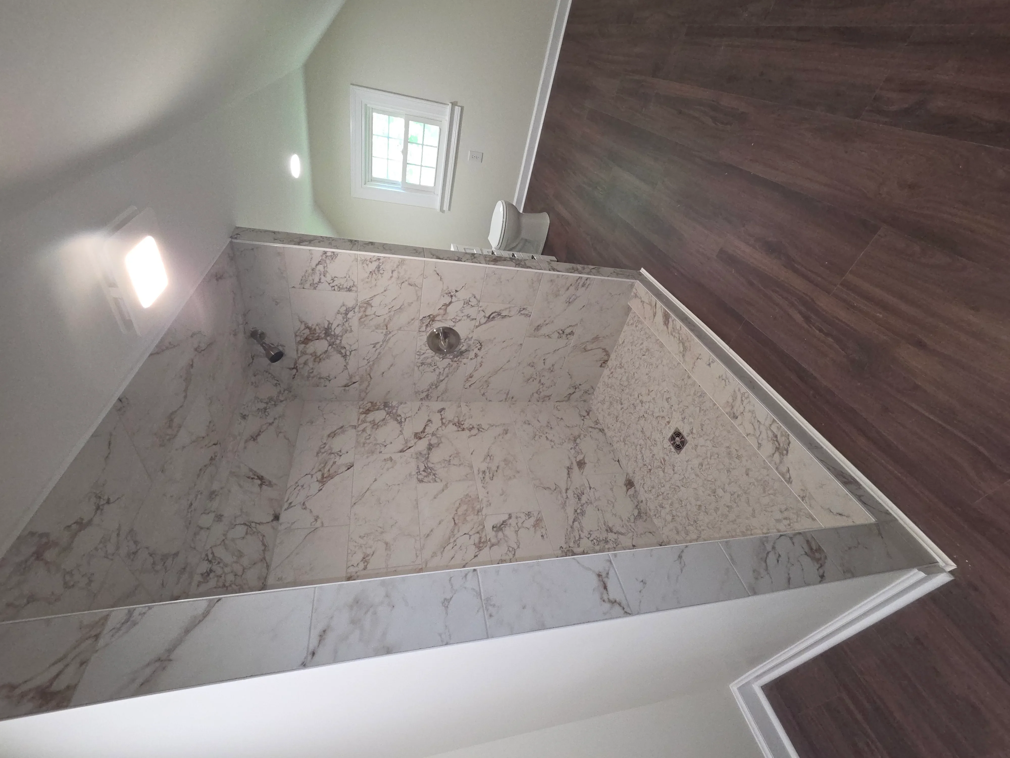 Marble tile shower surround with white trim and recessed lighting in renovated bathroom