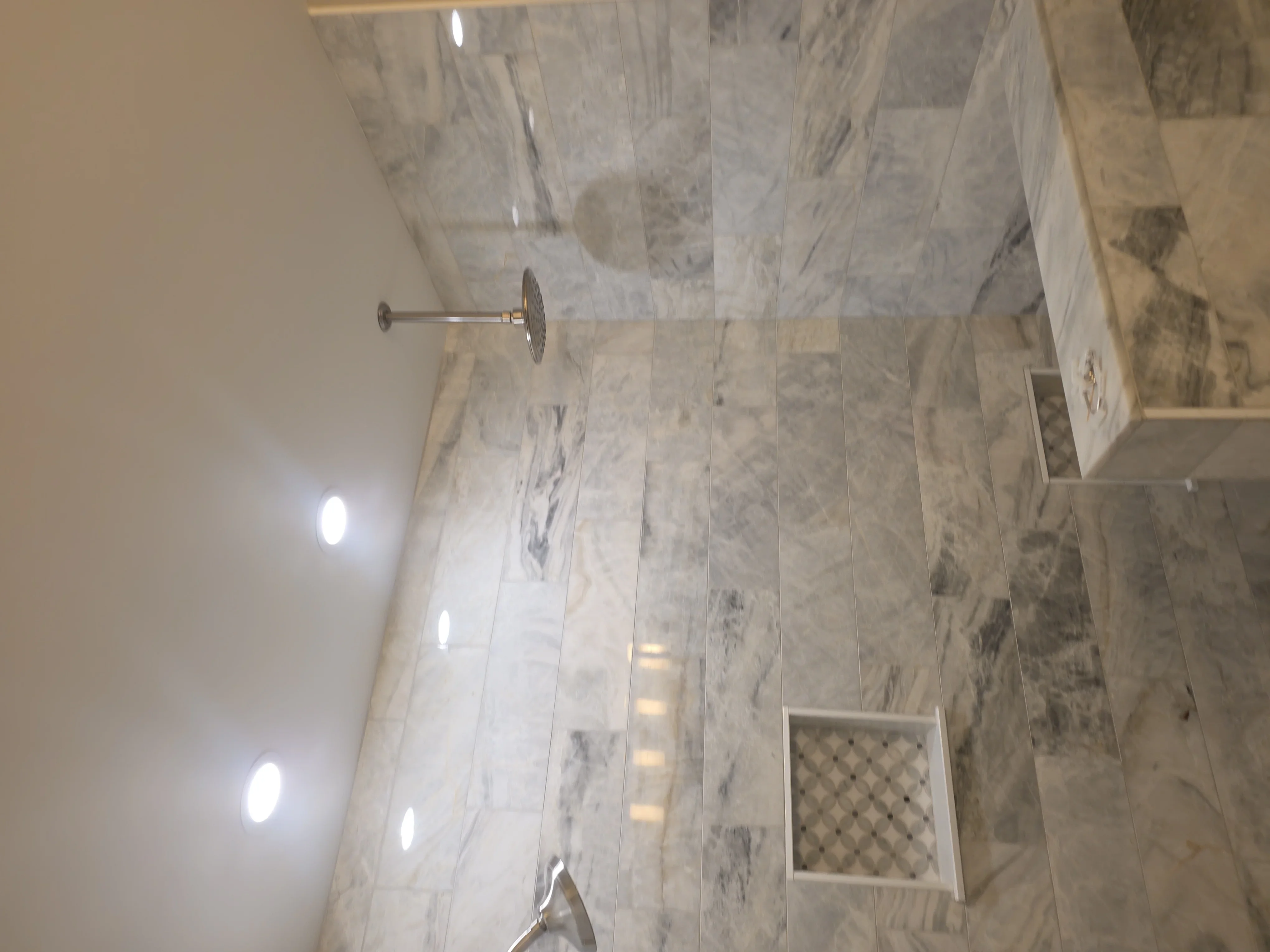 Marble tile shower with chrome fixtures and recessed lighting in bathroom remodel