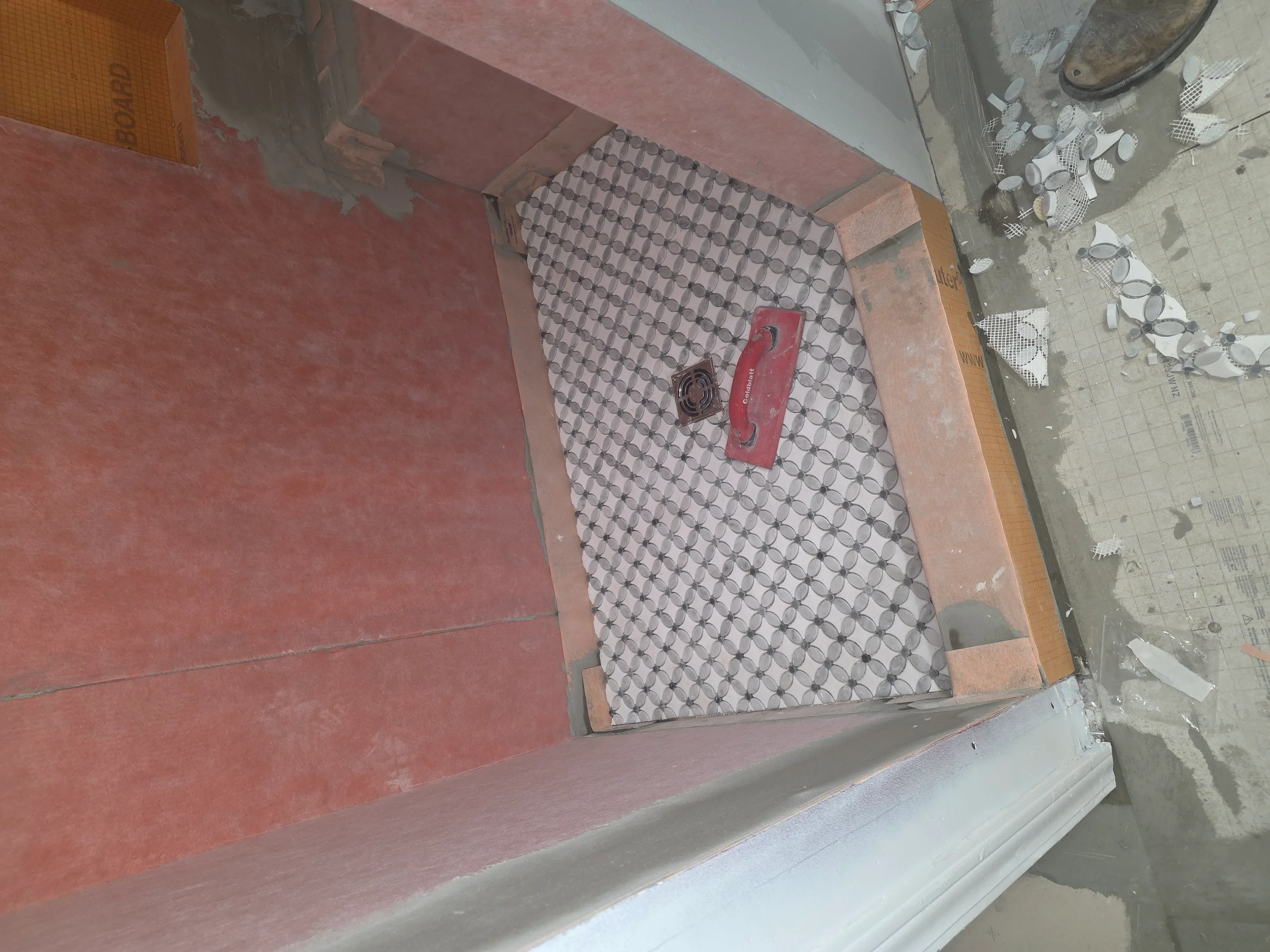 Geometric patterned bathroom floor tiles being installed with leveling tools visible